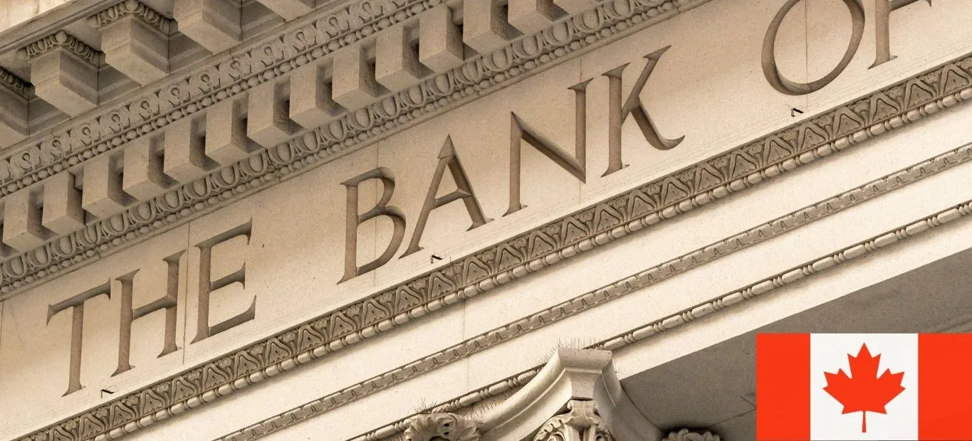 Close-up of an ornate stone bank facade engraved with "The Bank of", with a Canadian flag in the corner